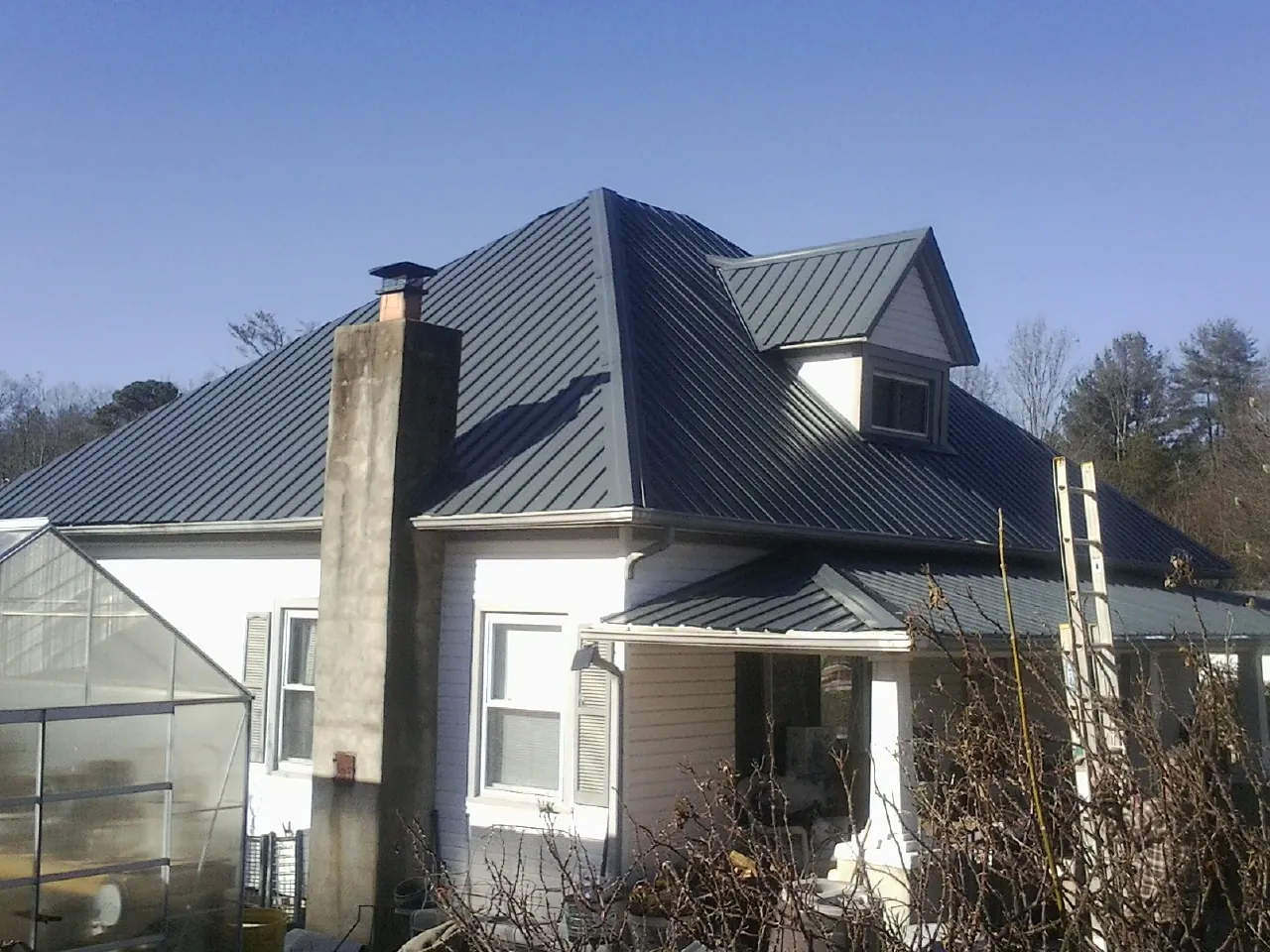 Dark blue standing seam metal roof on a white farmhouse with dormer — Slate & Tile Roof Repair by Roofing Brothers in Ricketts