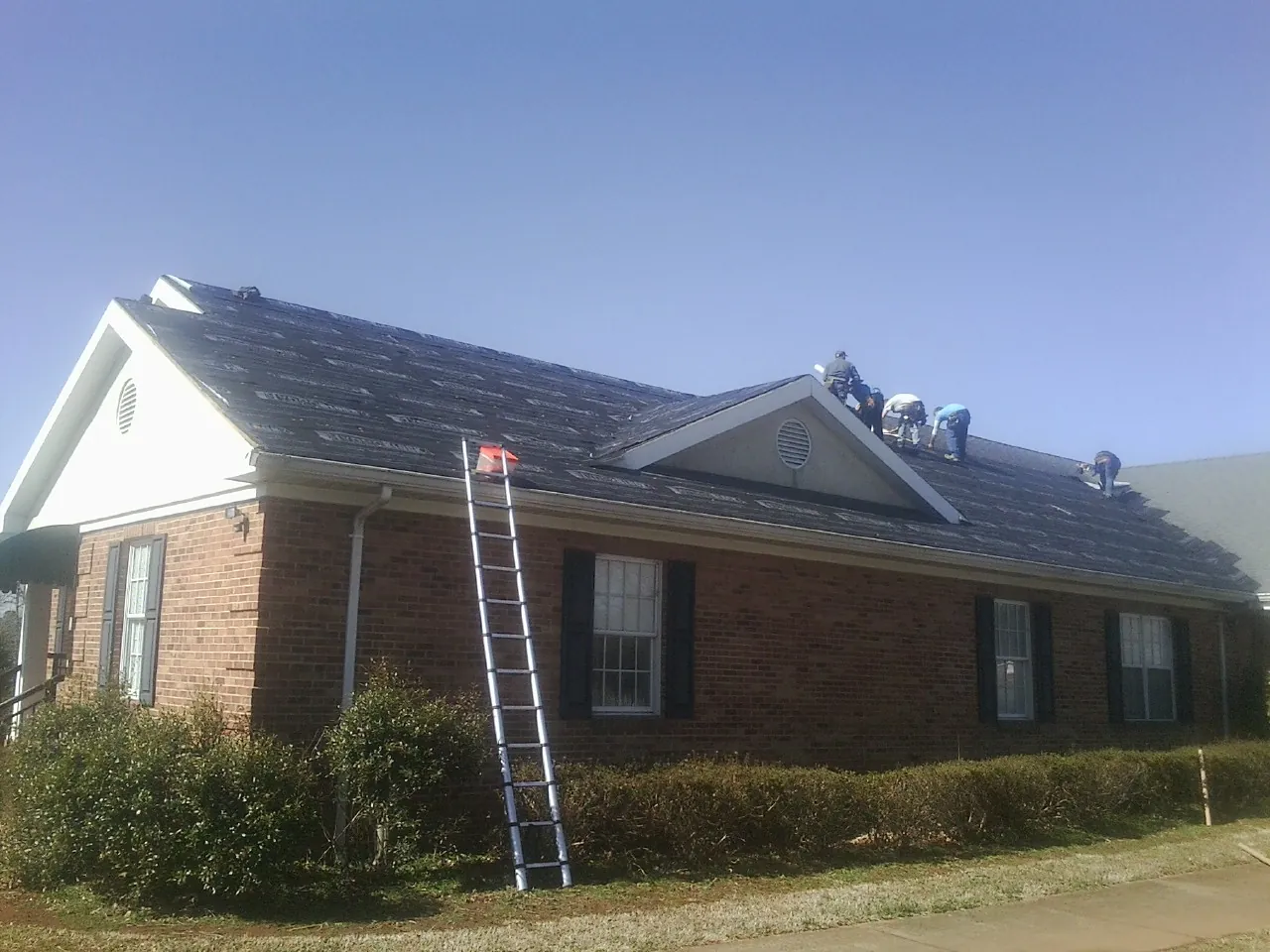 Crew tearing shingles off a brick ranch roof with a ladder set — Emergency Roof Repair work by our crew in Ricketts
