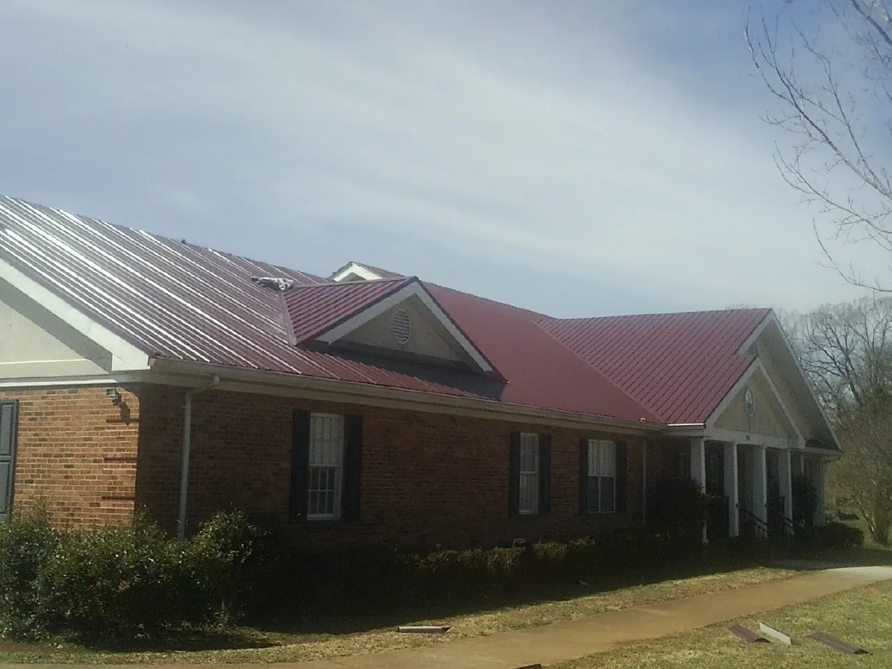 Red metal roof with gabled entries on a long brick building, from a Hail Damage Roof Repair job in Ricketts