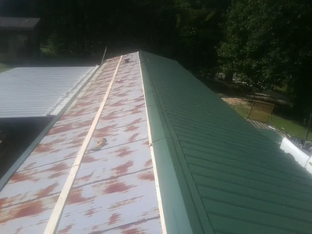Old rusted panels beside newly installed green metal roofing — Wind Damage Roof Repair by Roofing Brothers in Ricketts