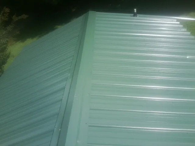 New green metal panels meeting at the ridge of a roof — Flat Roof Repair work by our crew in Ricketts