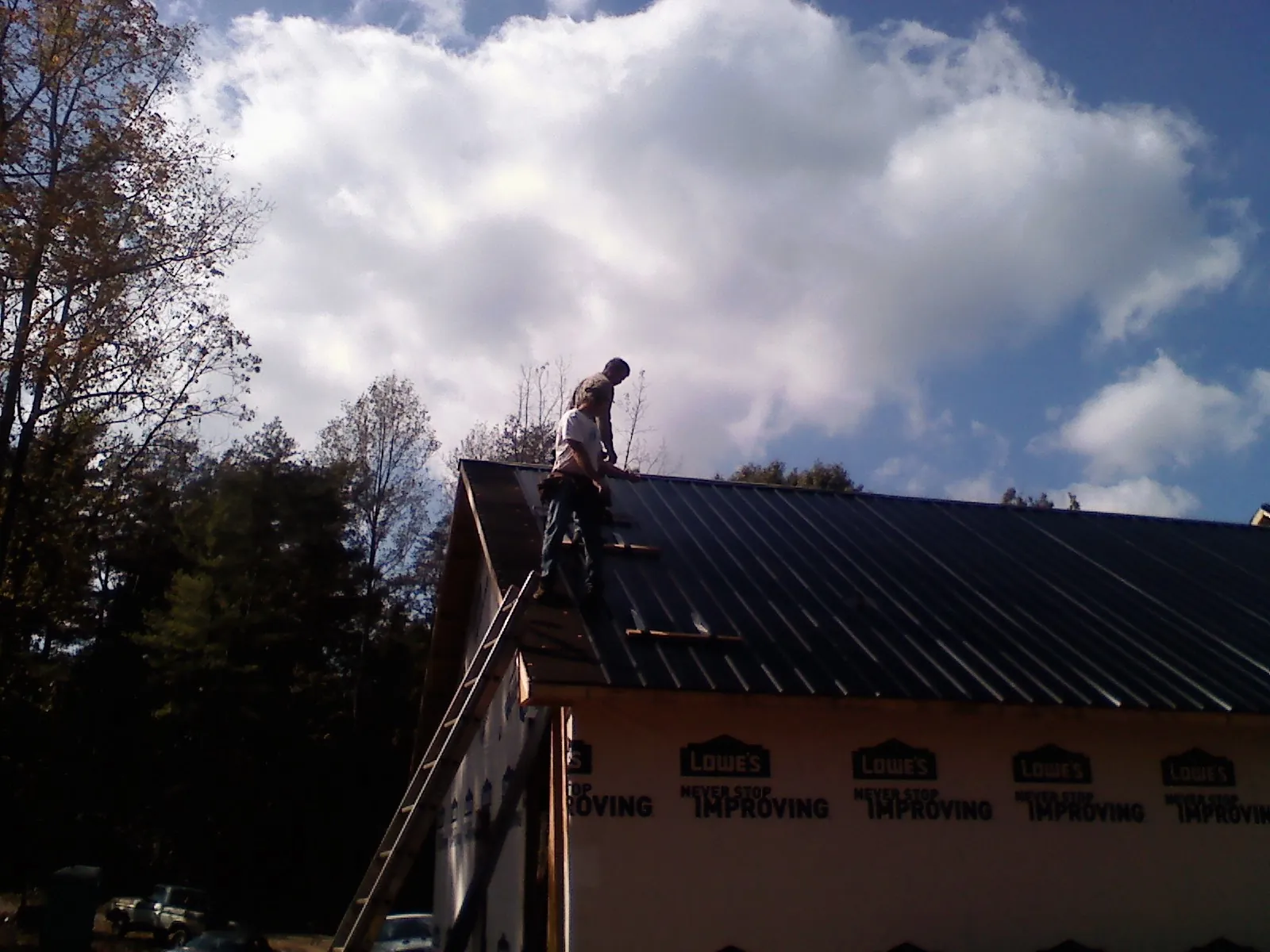 Roofer fastening dark metal panels high against a cloudy sky, from a Roof Inspection job in Ricketts