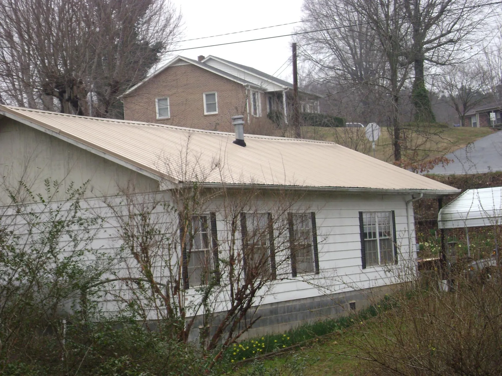 Tan metal roof on a white sided house set into a hillside — Commercial Roofing by Roofing Brothers in Ricketts