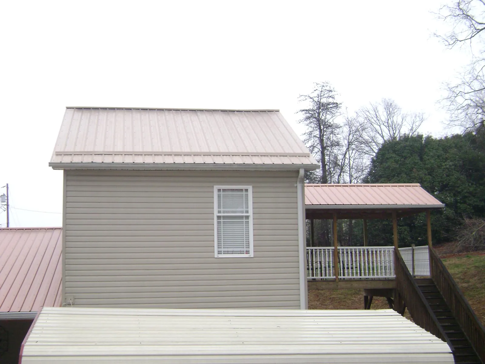 Tan metal roofs on a two story addition and attached porch, from a Roof Replacement job in Ricketts